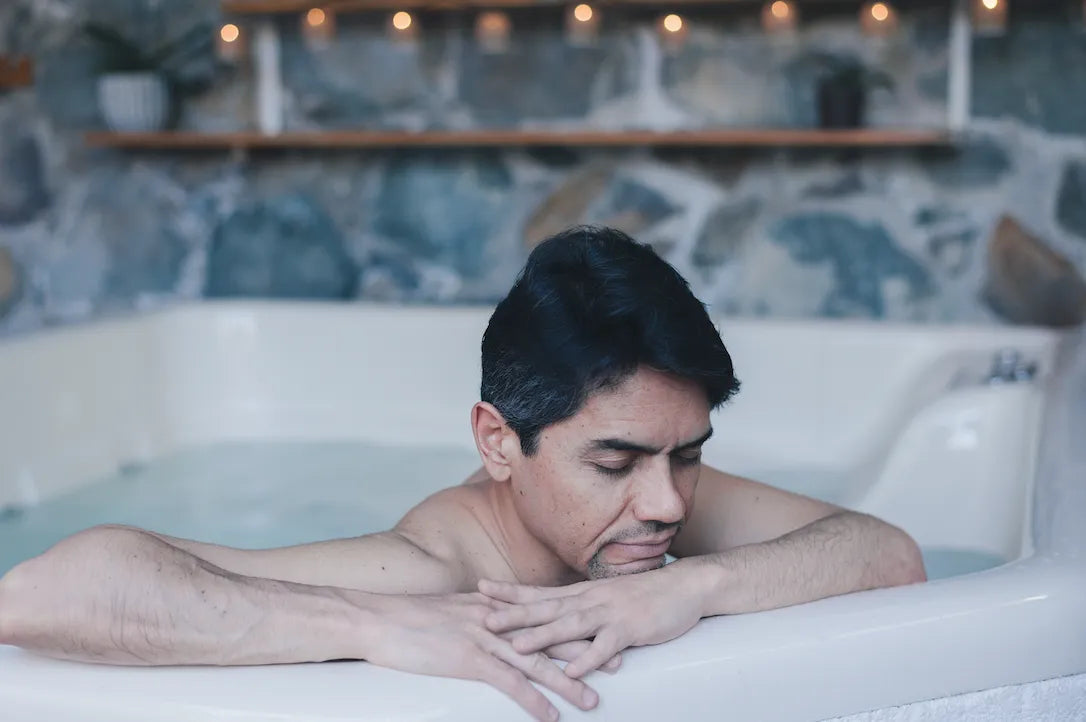 Man relaxing in a white hot tub with stone wall and wooden shelf background