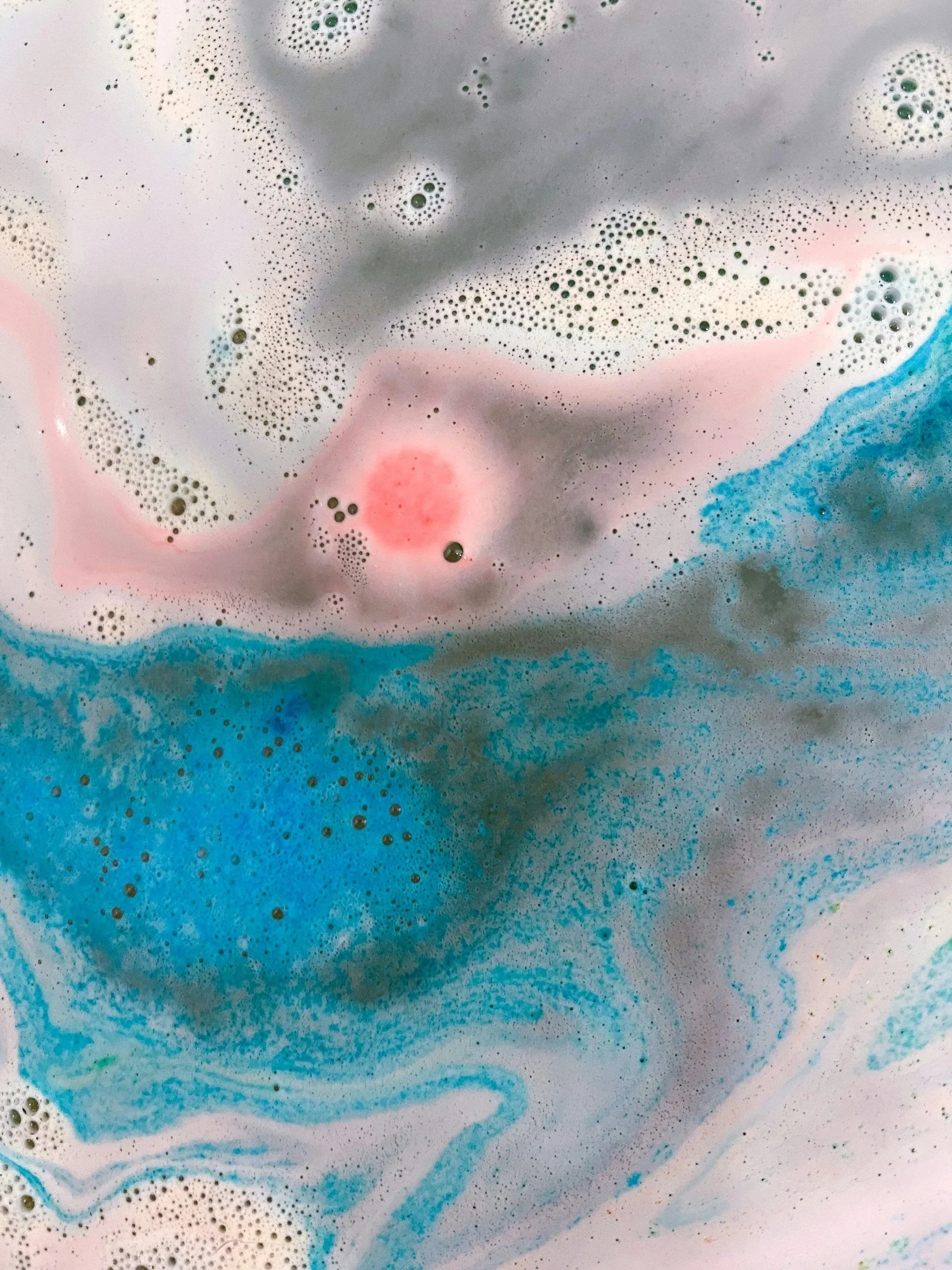 Close-up of colorful bath bomb foam with blue, pink, and white swirls and bubbles in water