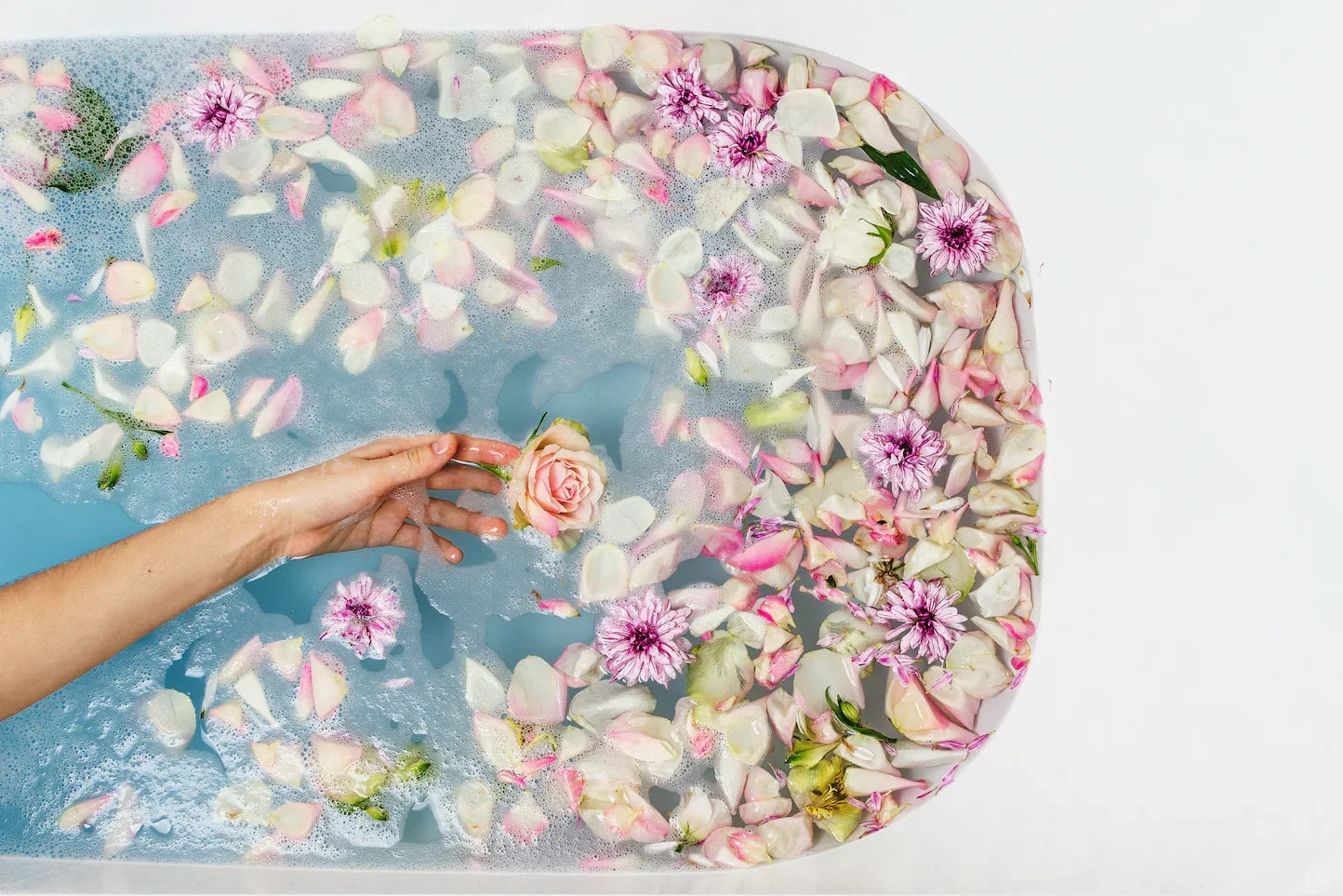 Hand holding a pink rose in a bubble bath filled with pink and white flower petals
