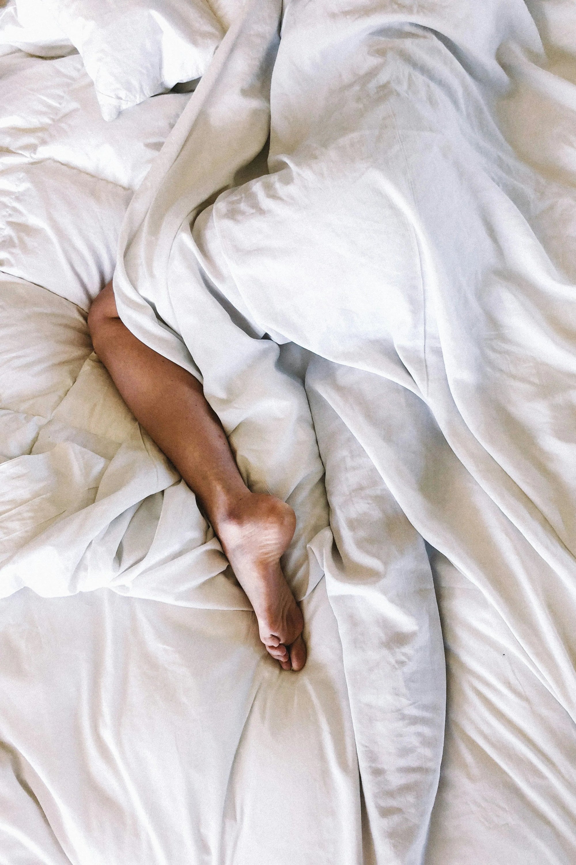 Person sleeping in bed with white sheets, one bare leg visible from under blanket