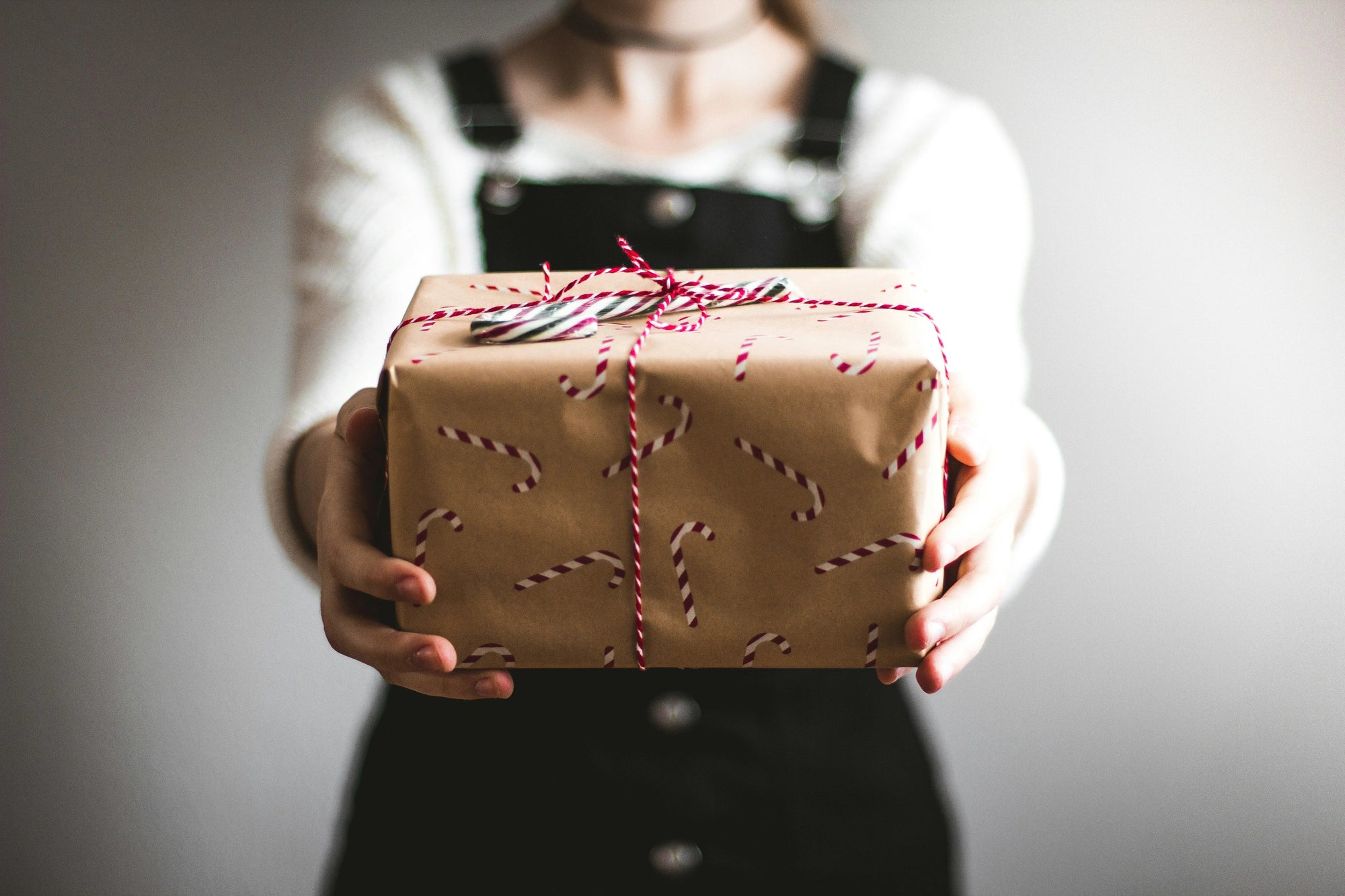 Person holding a wrapped gift box with candy cane patterned paper and a candy cane on top