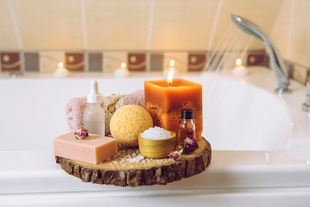 Spa bath scene with scented candle, bath bomb, soap, essential oils, and towel on wooden tray