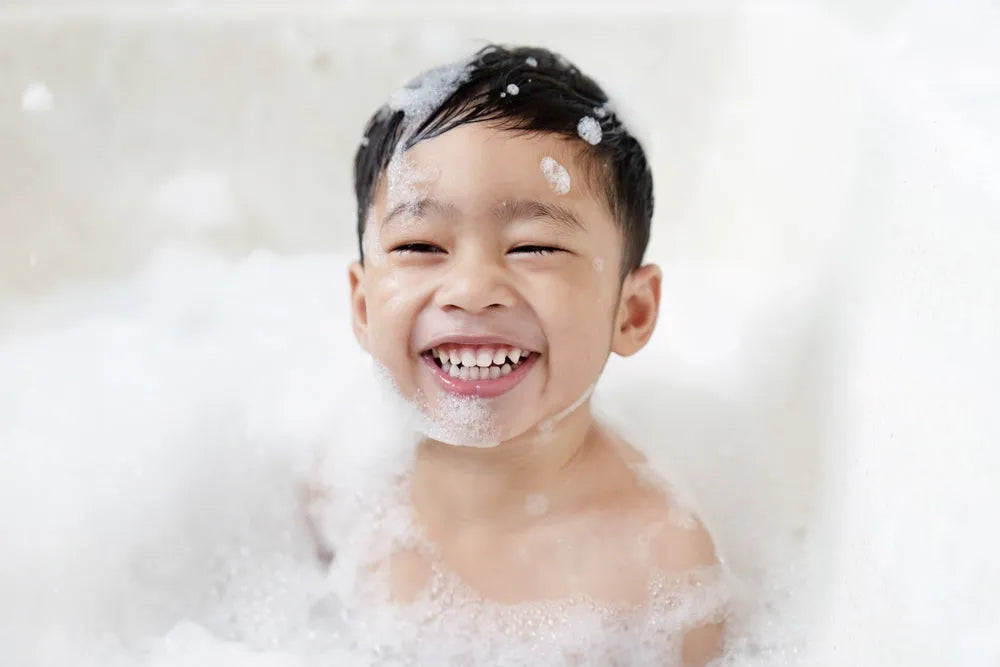 Smiling young boy enjoying a bubbly bath filled with white foam and soap bubbles