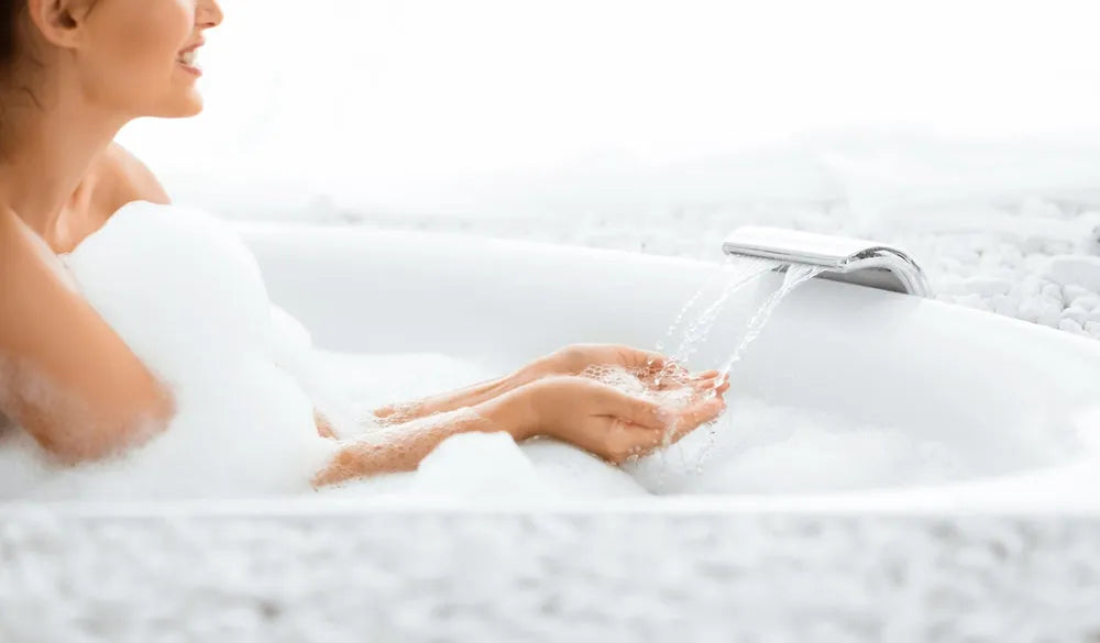 Woman enjoying a relaxing bubble bath with water flowing from a modern faucet in a white bathtub
