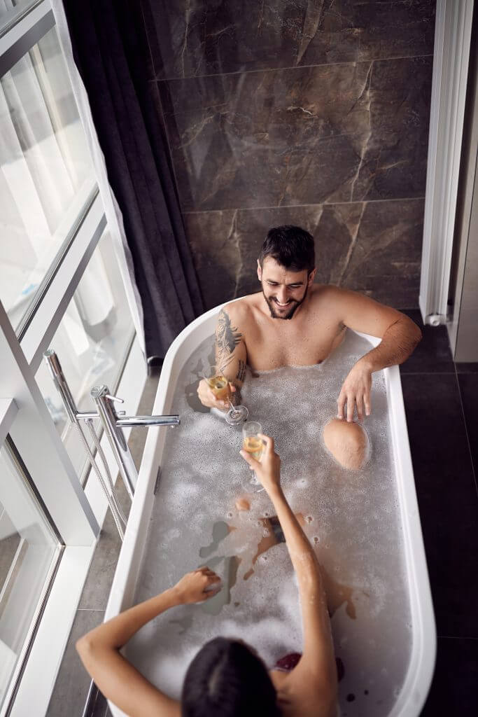Woman and man taking a bubble bath together while drinking wine
