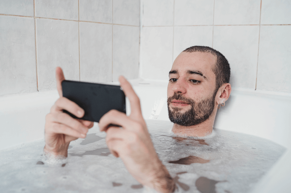 Man taking a bubble bath while holding his phone.